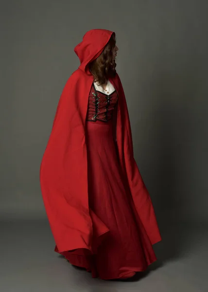 全长肖像画的女人穿着红色中世纪奇幻服装 头戴头巾飘逸 站立姿势侧写 手势手势 远离在灰色工作室背景下隔离的相机 — 图库照片