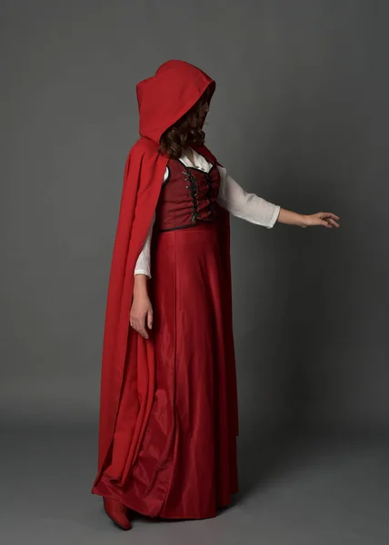 全长肖像画的女人穿着红色中世纪奇幻服装 头戴头巾飘逸 站立姿势侧写 手势手势 远离在灰色工作室背景下隔离的相机 — 图库照片