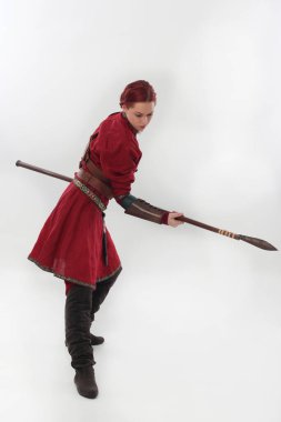 Kırmızı ortaçağ fantezi savaşçı kostümü giymiş, deri zırhlı, elinde silah olan güzel bir kadının tam boy portresi. Beyaz stüdyo arka planında izole edilmiş poz.