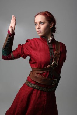  Güzel bir kadının portresi kırmızı ortaçağ fantezi savaşçı kostümü giymiş, deri zırhlı, elinde silah olan. Stüdyo arka planında izole edilmiş poz.