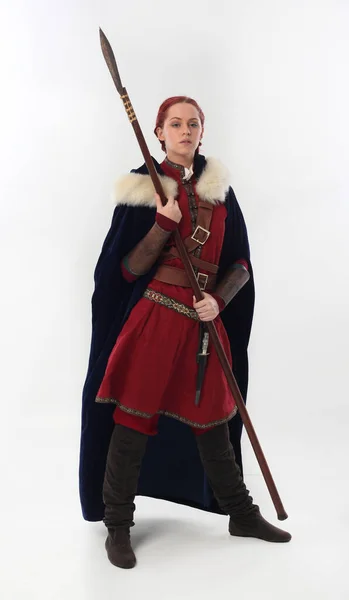 full length portrait of beautiful woman wearing a red medieval fantasy warrior costume with leather armour, holding weapons.  Standing pose isolated on white studio background.