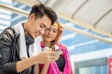 Genç Asyalı çiftler egzersiz, rahatlama, mutluluk, cep telefonları ve kulaklıklardan hoşlanıyorlar, müzik dinliyorlar ve akıllı yapay zeka teknolojisi ile sağlıklarını kontrol ediyorlar, seçici odaklı kadın.