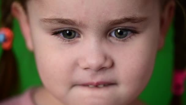 Маленька дівчинка блимає очима, повільний рух дитини, портрет на зеленому тлі . — стокове відео