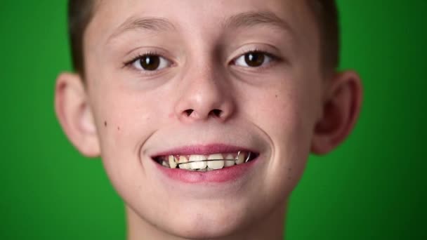 Dziecko wkłada płytkę dentystyczną do osiowania krzywych zębów, portret dziecka na zielonym tle. — Wideo stockowe