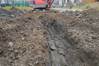 Bir kazıcı yol boyunca kanalizasyon ve yağmur suyu için bir çukur kazıyor, bir sürüngen kazıcı..