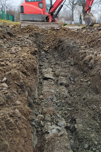 Uma escavadora cava uma trincheira para esgoto e água da chuva ao longo do lado da estrada. — Fotografia de Stock
