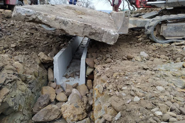 Экскаватор устанавливает бетонные поддоны для осушения дождевой воды в сельской местности, бетонные изделия для осушения воды. — стоковое фото