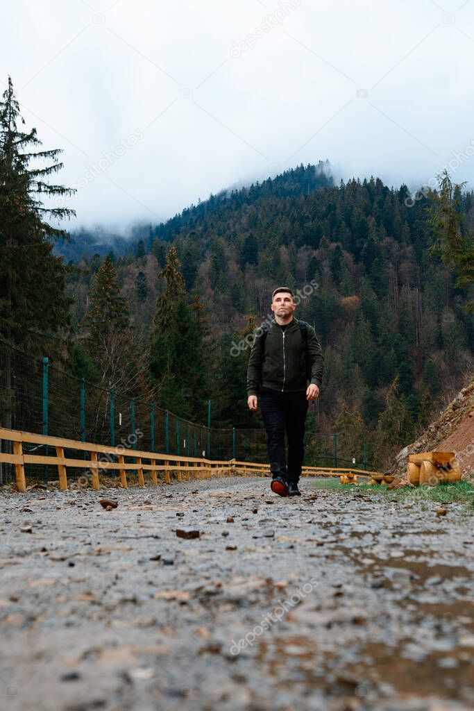 Walking on forest roads, a man walking alone on a forest road against the backdrop of a mountain top with fog, the road is fenced.