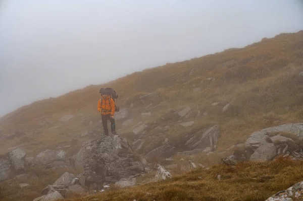 ハイキングのためのバックパックを持つ男は岩の道で山の頂上に登り ウクライナのカルパティアの観光客 霧の中の観光客 — ストック写真