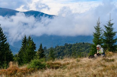 Thyrist dağların arka planında oturur ve dinlenir, bir köpek yakınlarda koşar, sonbahar manzaraları, bulutlu dağlar.