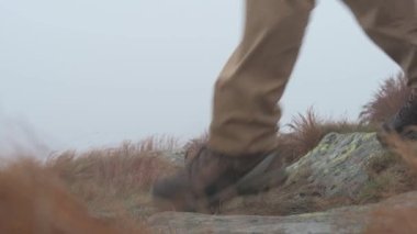 Hiker in boots walking on a stone road against the background of fog and mountain stones.