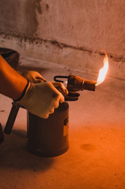 Gasoline blowtorch with a burning fire, the use of a blowtorch in construction, a man's hand in a glove.