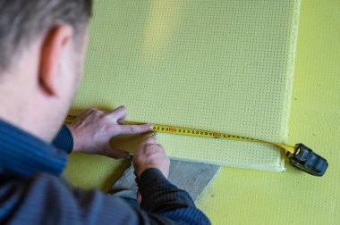 The master measures the length of expanded polystyrene on the floor, installation and insulation of the floor in the room, expanded polystyrene.
