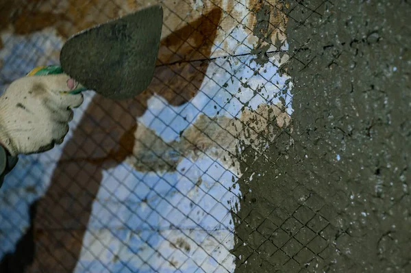 The master throws a solution of liquid concrete on the wall, the first layer of plaster on the wall, metal mesh attached to a wooden wall.