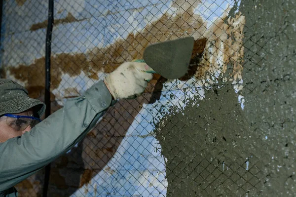 The master throws a solution of liquid concrete on the wall, the first layer of plaster on the wall, metal mesh attached to a wooden wall.