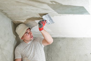 Eldivenli usta kireç alçısıyla tavanı eşitliyor. Odayı kendi elleriyle onarıyor..