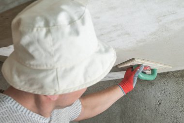 Kireç alçısını nemlendirici süngerle düzleştirirken, usta tavanı inşaat rendesiyle ovuyor..