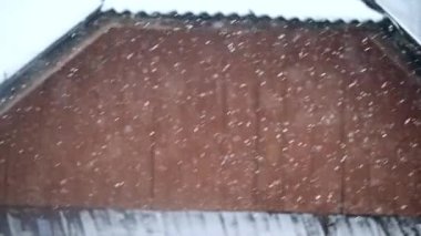 Kış günü kar tanelerinin etrafında bulanık düşüşler, günün kırmızı çatısının arka planında kar, yavaş çekim video. .