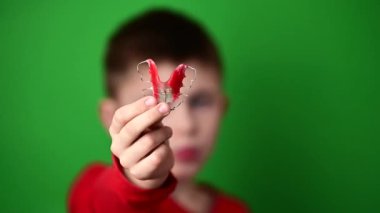 Dişleri hizalamak için plaka, yeşil arka planda elinde plaka, elinde takma diş plakası olan bir çocuk. yeni