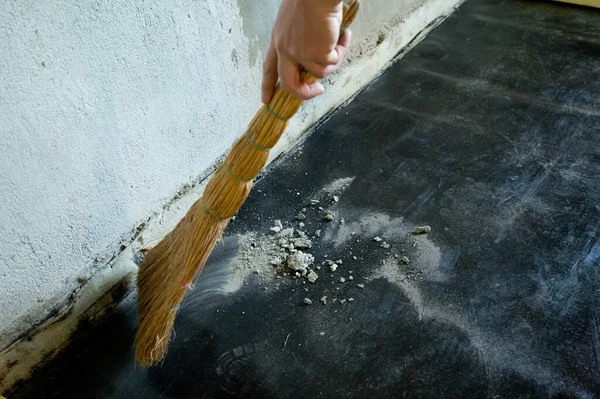 A worker sweeps construction debris with a broom, gunpowder and small particles of concrete.