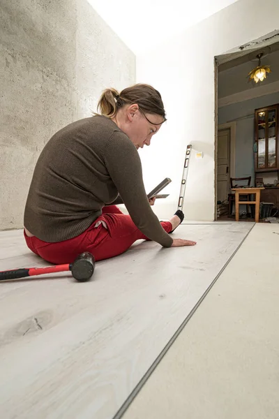 Installing a quartz vinyl floor, a woman performs installation work, installing a floor with a hammer and angle.