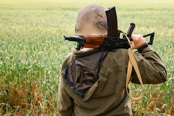 A soldier with a machine gun stands in a field, Ukrainian wheat fields and war, a woman warrior with a machine gun.