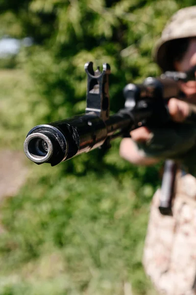 A soldier with a combat military assault rifles AK 74 stands in a field, Ukrainian wheat fields and war, muzzle brake compensator and sight of the automatic machine.