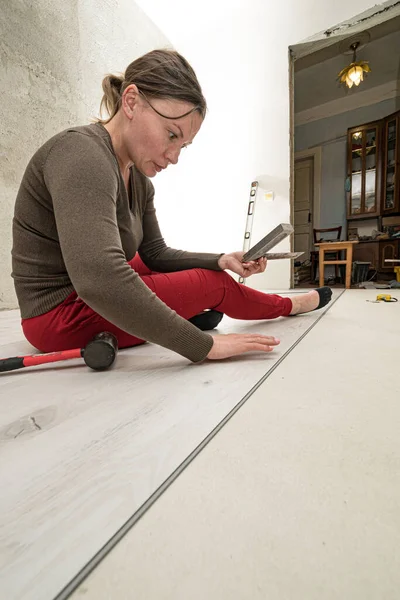 Installing a quartz vinyl floor, a woman performs installation work, installing a floor with a hammer and angle.