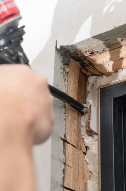 Bir adam eliyle sprey tabanca kullanır ve boşluğu yeni ahşap bir kapı ile duvar arasındaki inşaat köpüğüyle doldurur..