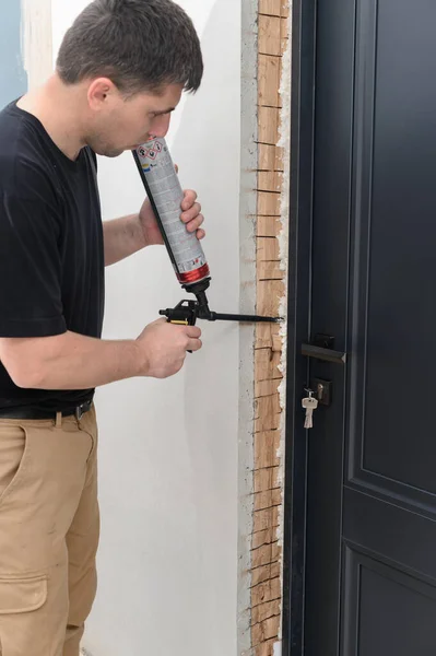 a man uses a spray gun with his hand and fills the gap with construction foam between a new wooden door and a wall, the process of installing a door.