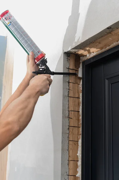 a man uses a spray gun with his hand and fills the gap with construction foam between a new wooden door and a wall, the process of installing a door.