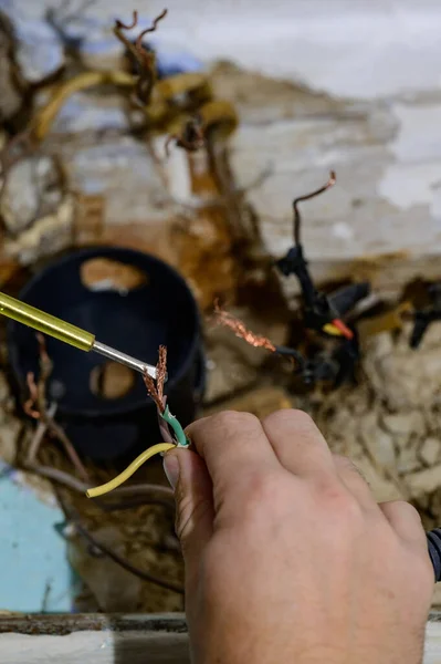 Old electrical wiring in the house, wooden walls in the house, replacement of electrical cables, the master checks the old wire for contact with electricity.