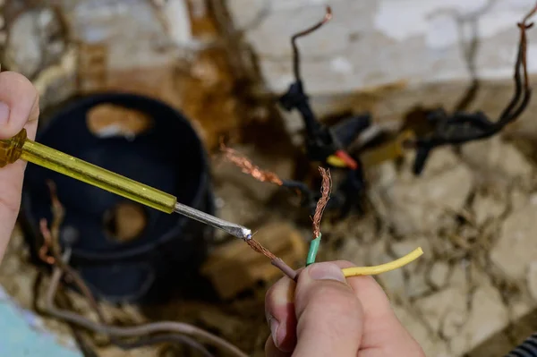 Old electrical wiring in the house, wooden walls in the house, replacement of electrical cables, the master checks the old wire for contact with electricity.