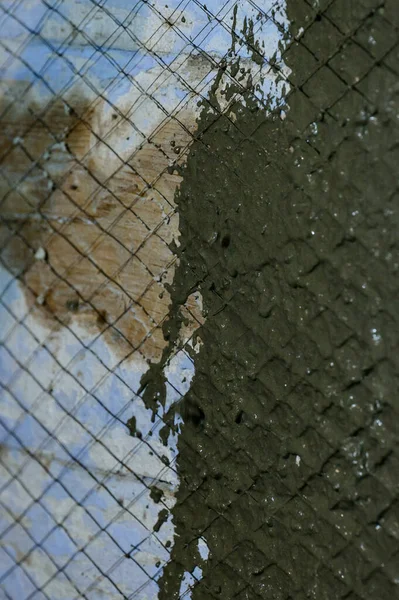 The master throws a solution of liquid concrete on the wall, the first layer of plaster on the wall, metal mesh attached to a wooden wall.