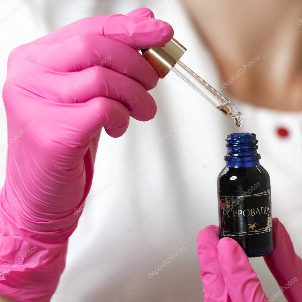 Ivano-Frankivsk, Ukraine July 27, 2022: a beautician holds in his hands a serum for cleansing and moisturizing the face, a drop of serum and a beautician in the background.