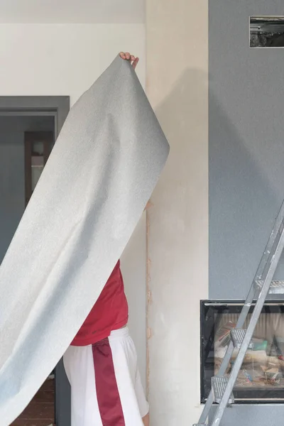 A man glues wallpaper on a wall in a house, a craftsman uses a ladder to glue wallpaper on top.