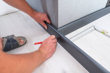 Wooden plinth in the room, installation of the plinth by a master carpenter, the master draws a pencil mark on the plinth.