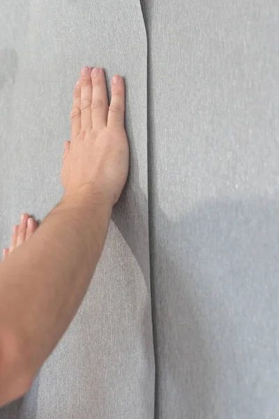 A man glues vinyl wallpaper on the wall, repair in the room and wallpapering, gray wallpaper.