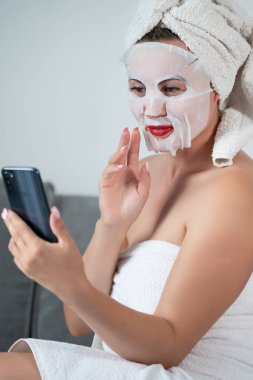 Facial skin cleansing procedure using a cosmetic mask, woman talking on the phone online, women's tricks and beauty.
