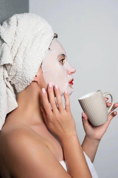 Fabric face mask, moisturizing mask for facial skin, girl holding a cup in her hands.