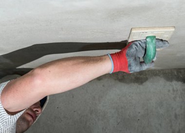 Kireç alçısını nemlendirici süngerle düzleştirirken, usta tavanı inşaat rendesiyle ovuyor..