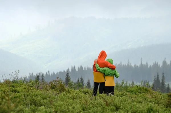 Two boys of school age are hugging and admiring the view of the Carpathians, children in bright clothes with seats in the mountains.