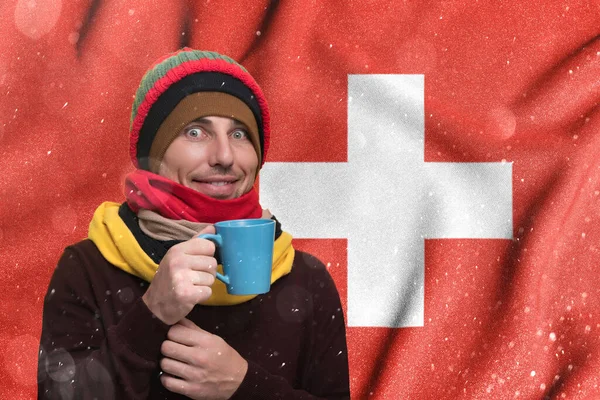 Switzerland and the gas winter crisis, high gas tariffs for the population, a smiling man warms himself with a cup of tea and warm clothes.