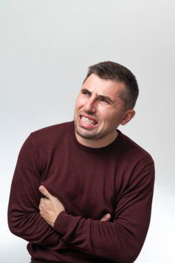 A man touches his stomach with two hands, on a white background with copy space, Stomach pain in a man, unbearable abdominal pain.