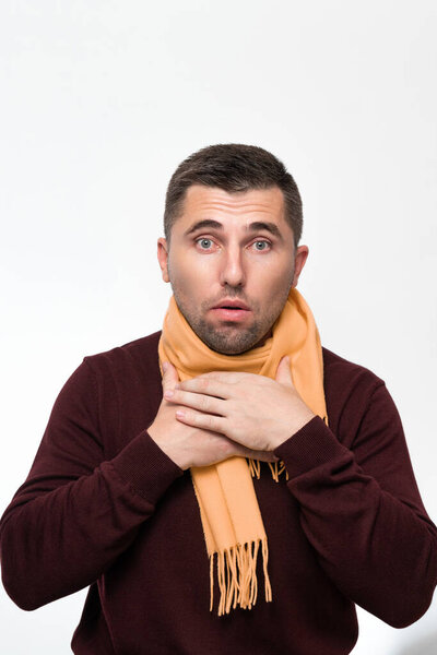 A man suffers from a sore throat, a man wrapped his throat with a scarf, portrait on a white background, severe sore throat.