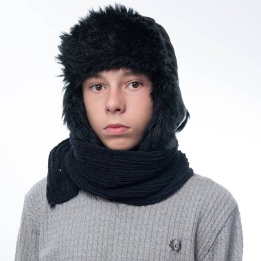 Portrait of a child in a winter hat with earflaps and a knitted scarf on a white background, black winter clothes.