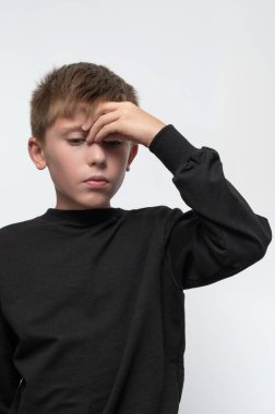 A child has a headache, a boy holds his hand on his forehead from a headache, a headache in childhood.