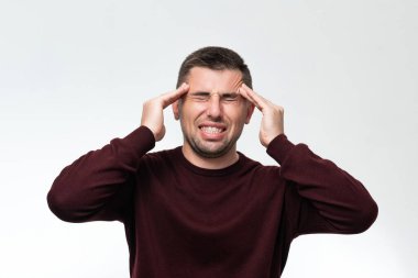 A handsome man wearing a casual sweater feels tired and has a headache, Stress and headache concept, severe headache, hands near the pulse of the head.