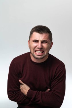 A man touches his stomach with two hands, on a white background with copy space, Stomach pain in a man, unbearable abdominal pain.