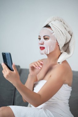 Facial skin cleansing procedure using a cosmetic mask, woman talking on the phone online, women's tricks and beauty.